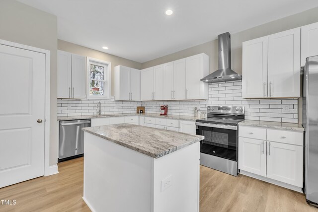 kitchen with a sink, white cabinetry, appliances with stainless steel finishes, light wood-type flooring, and wall chimney exhaust hood