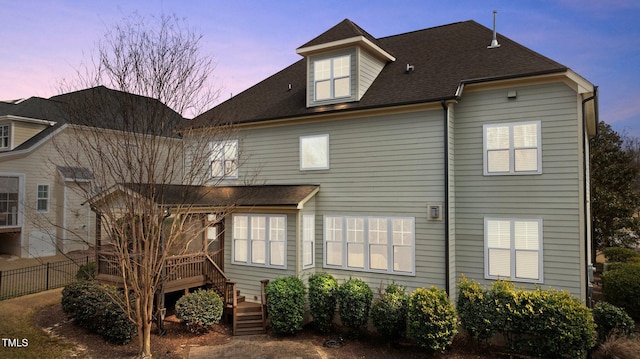 back of property at dusk featuring a deck, fence, and roof with shingles