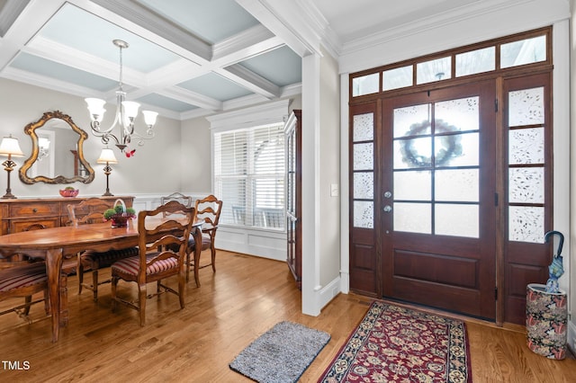 entrance foyer with beam ceiling, a notable chandelier, ornamental molding, coffered ceiling, and light wood-style floors