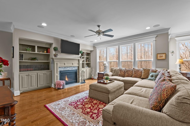 living room with built in shelves, ornamental molding, recessed lighting, light wood-style floors, and a fireplace