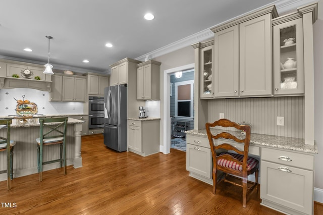 kitchen featuring a kitchen breakfast bar, wood finished floors, appliances with stainless steel finishes, glass insert cabinets, and built in study area