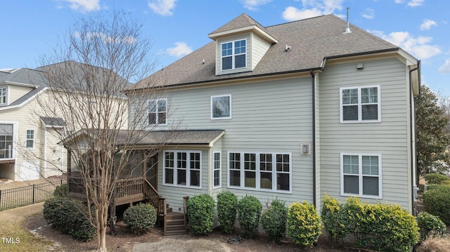 rear view of house featuring roof with shingles, a deck, and fence