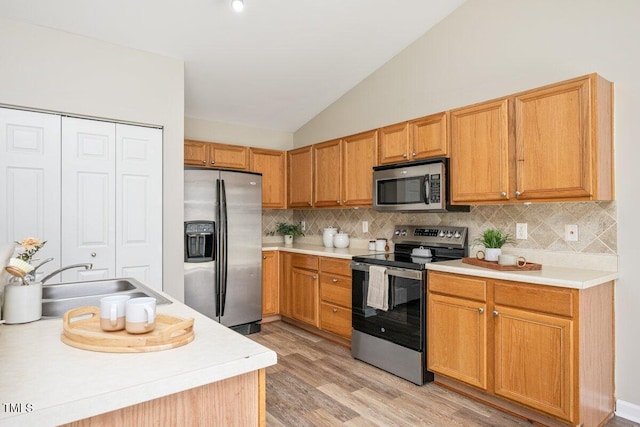 kitchen featuring lofted ceiling, light wood-style flooring, light countertops, appliances with stainless steel finishes, and tasteful backsplash