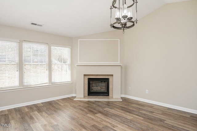 unfurnished living room with a tiled fireplace, vaulted ceiling, wood finished floors, and baseboards