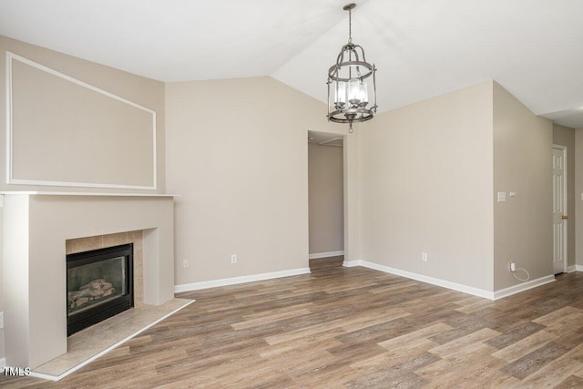 unfurnished living room with a tile fireplace, baseboards, lofted ceiling, and wood finished floors