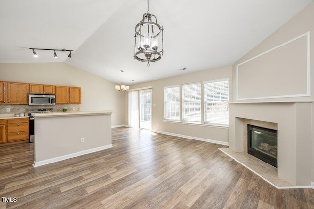 kitchen featuring brown cabinetry, an inviting chandelier, vaulted ceiling, appliances with stainless steel finishes, and a glass covered fireplace