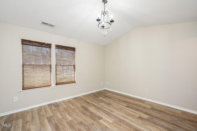 empty room with visible vents, baseboards, lofted ceiling, an inviting chandelier, and wood finished floors