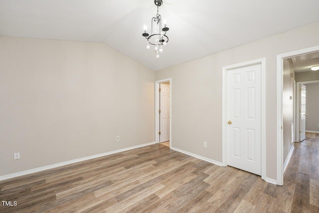 unfurnished bedroom with a notable chandelier, baseboards, lofted ceiling, and wood finished floors