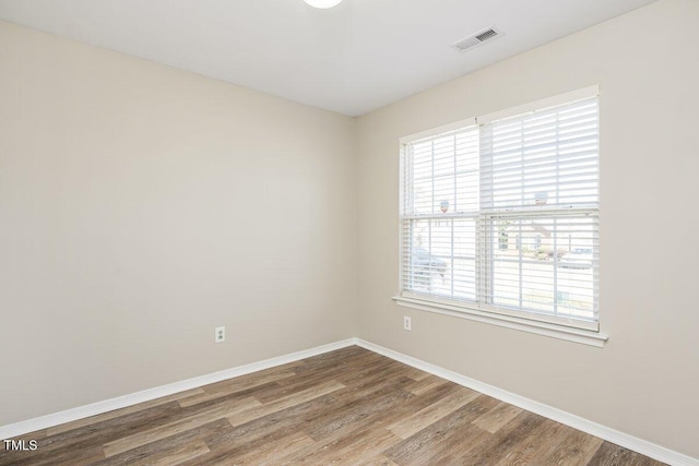 unfurnished room featuring wood finished floors, visible vents, and baseboards