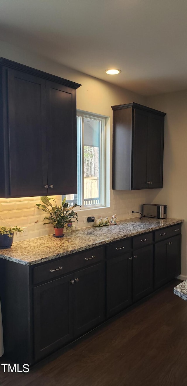 kitchen with dark wood-style floors, backsplash, dark cabinetry, and light stone countertops