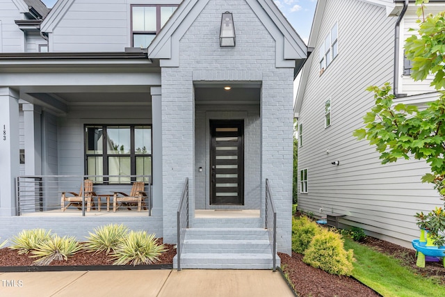 entrance to property featuring a porch and brick siding