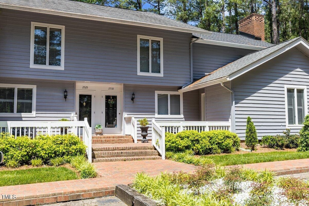 view of front of property with a porch, roof with shingles, and a chimney