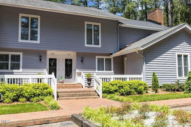 view of front of property with a porch, roof with shingles, and a chimney