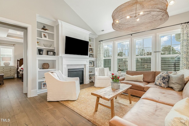 living room with a glass covered fireplace, built in features, a healthy amount of sunlight, and wood-type flooring