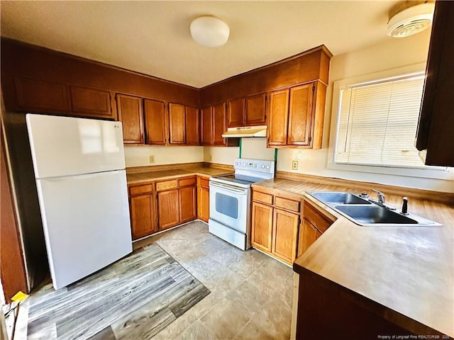 kitchen featuring electric range oven, brown cabinets, freestanding refrigerator, under cabinet range hood, and a sink