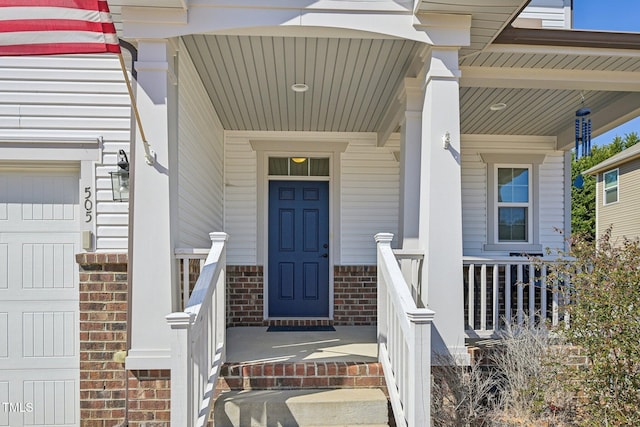 doorway to property with brick siding, covered porch, and an attached garage