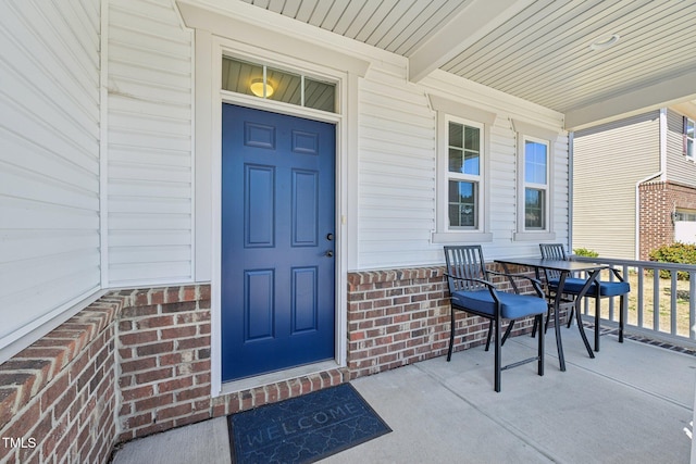 view of exterior entry with brick siding, a porch, and outdoor dining area