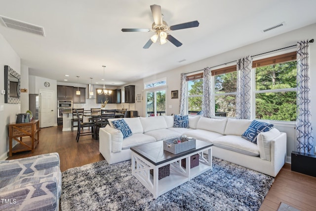 living room featuring visible vents, dark wood-style floors, and ceiling fan with notable chandelier