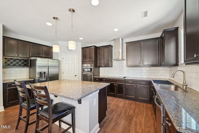 kitchen with wall chimney range hood, dark wood-style floors, stainless steel appliances, and a sink