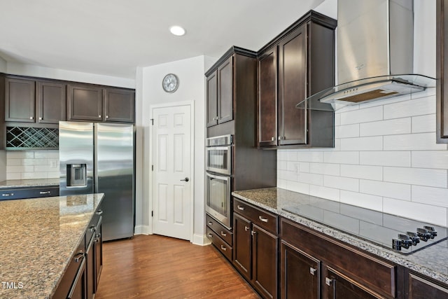 kitchen featuring dark stone counters, dark wood-type flooring, appliances with stainless steel finishes, and wall chimney exhaust hood