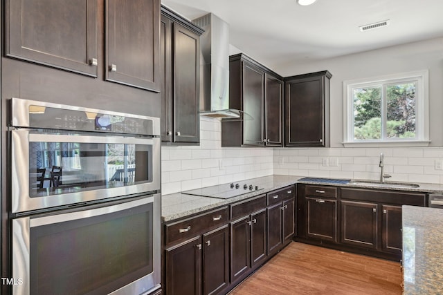 kitchen featuring visible vents, stainless steel double oven, a sink, wall chimney exhaust hood, and black electric cooktop