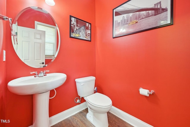 half bath featuring toilet, wood finished floors, baseboards, and a sink