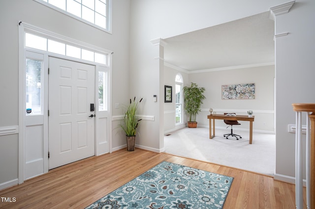 entryway with ornamental molding, a towering ceiling, baseboards, and wood finished floors