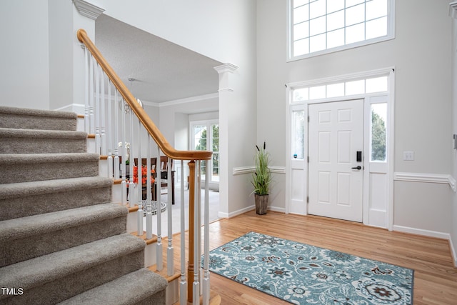 entrance foyer with baseboards, a towering ceiling, wood finished floors, stairs, and crown molding