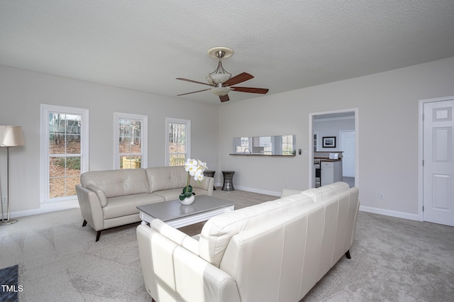 living room with light carpet, a textured ceiling, a ceiling fan, and baseboards