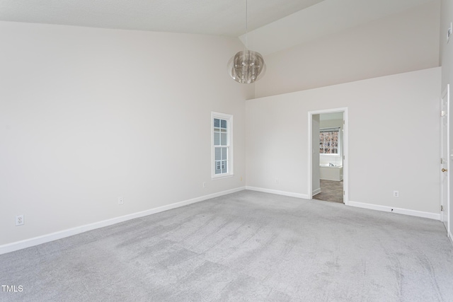 carpeted empty room with a notable chandelier, high vaulted ceiling, and baseboards