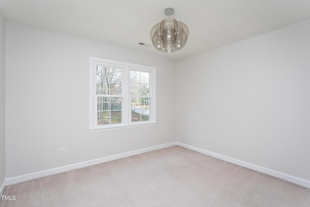 spare room featuring visible vents, an inviting chandelier, light carpet, a textured ceiling, and baseboards