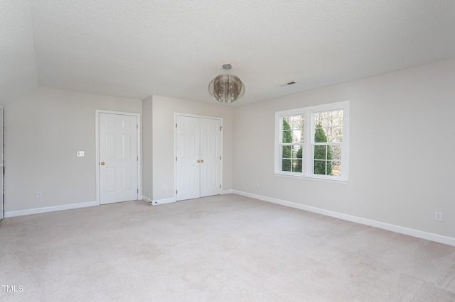 unfurnished bedroom featuring light carpet, a textured ceiling, a closet, and baseboards