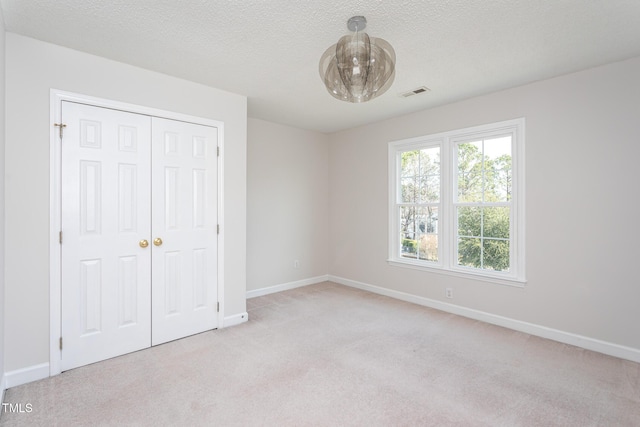 unfurnished bedroom featuring a textured ceiling, baseboards, visible vents, and light colored carpet