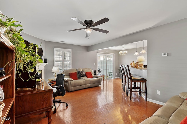 living room featuring plenty of natural light, ceiling fan with notable chandelier, a fireplace, and wood finished floors