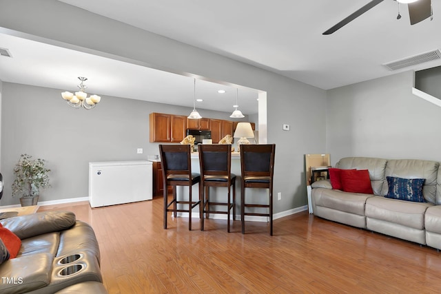 living area with light wood-style flooring, visible vents, baseboards, and ceiling fan with notable chandelier