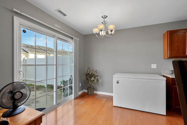 interior space featuring cabinet space, baseboards, visible vents, light wood-style flooring, and a notable chandelier