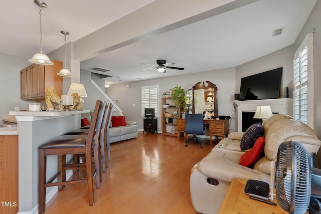 living room with ceiling fan, a fireplace, visible vents, and light wood-style floors