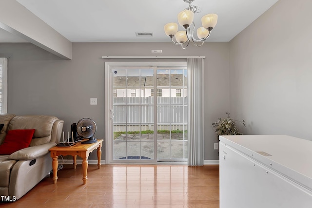 interior space featuring baseboards, visible vents, light wood finished floors, and an inviting chandelier