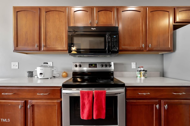 kitchen featuring black microwave, light countertops, stainless steel range with electric stovetop, and brown cabinets