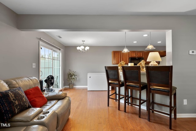 kitchen with baseboards, open floor plan, light wood-type flooring, black microwave, and a kitchen bar