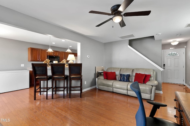 living room featuring ceiling fan, light wood finished floors, visible vents, and baseboards