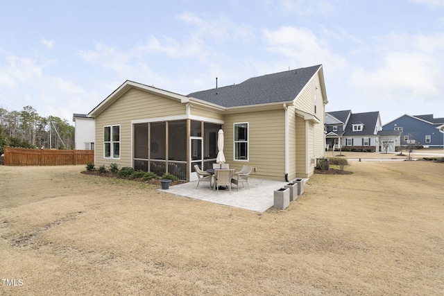 rear view of property featuring a patio area, a shingled roof, fence, and a sunroom