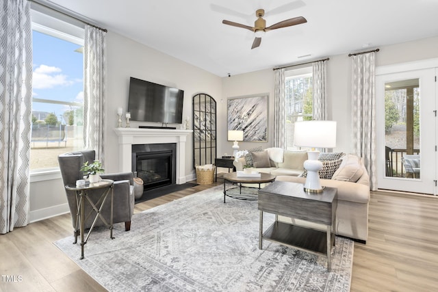 living room with a fireplace with flush hearth, ceiling fan, wood finished floors, and baseboards