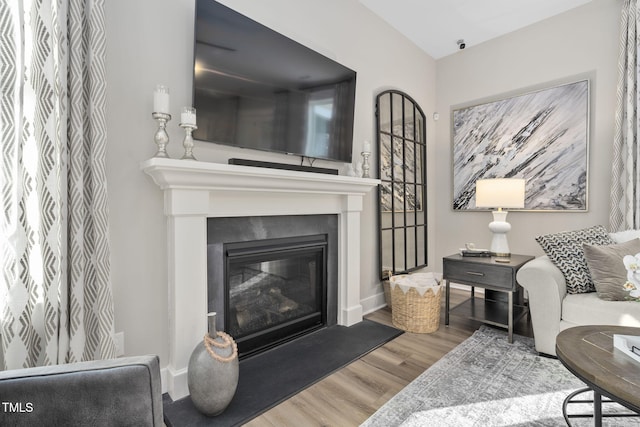 living room featuring a glass covered fireplace, baseboards, and wood finished floors