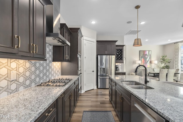 kitchen with appliances with stainless steel finishes, a sink, wall chimney exhaust hood, and light stone countertops