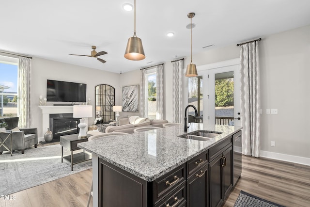 kitchen featuring a sink, baseboards, light wood-style floors, a glass covered fireplace, and pendant lighting