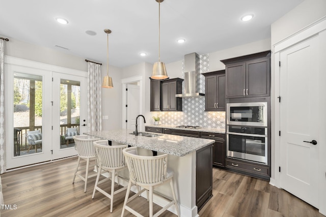 kitchen with dark wood-style floors, backsplash, appliances with stainless steel finishes, a sink, and wall chimney range hood