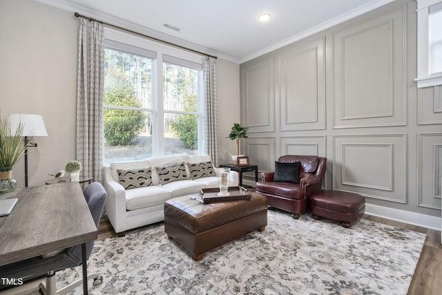 living area with visible vents, crown molding, a decorative wall, and wood finished floors