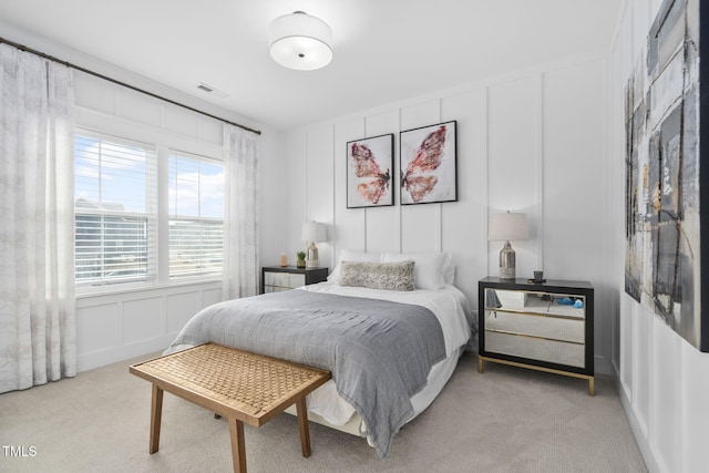 bedroom featuring light carpet, a decorative wall, and visible vents