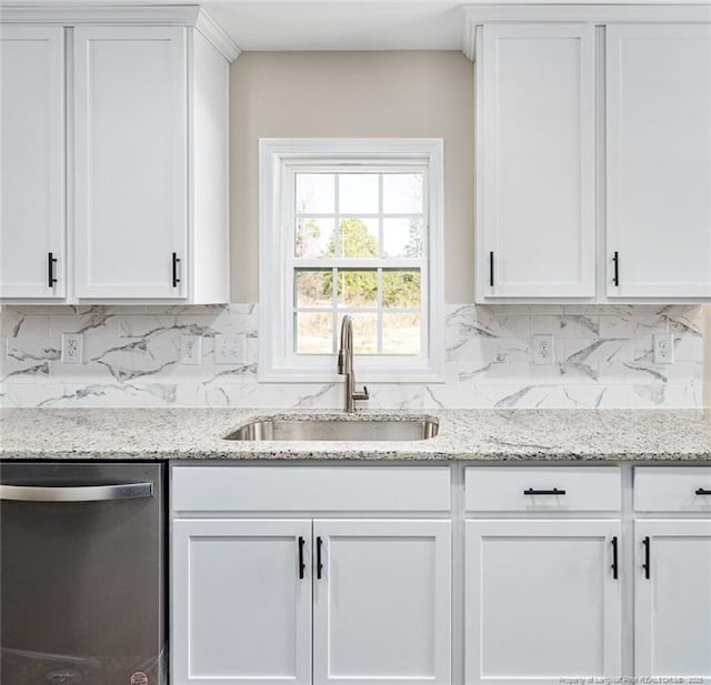 kitchen featuring tasteful backsplash, white cabinets, light stone countertops, stainless steel dishwasher, and a sink